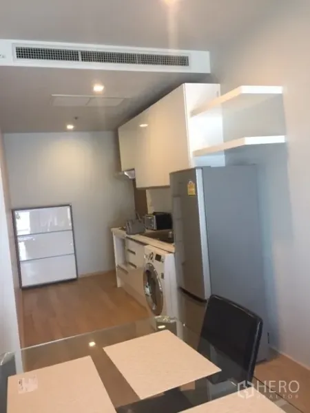 คอนโด ให้เช่าในBangkok - ครัวแบบแกลเล่ย์ตู้สีขาว พร้อมตู้เย็น ไมโครเวฟ และเครื่องซักผ้า ถัดจากโต๊ะทานอาหาร