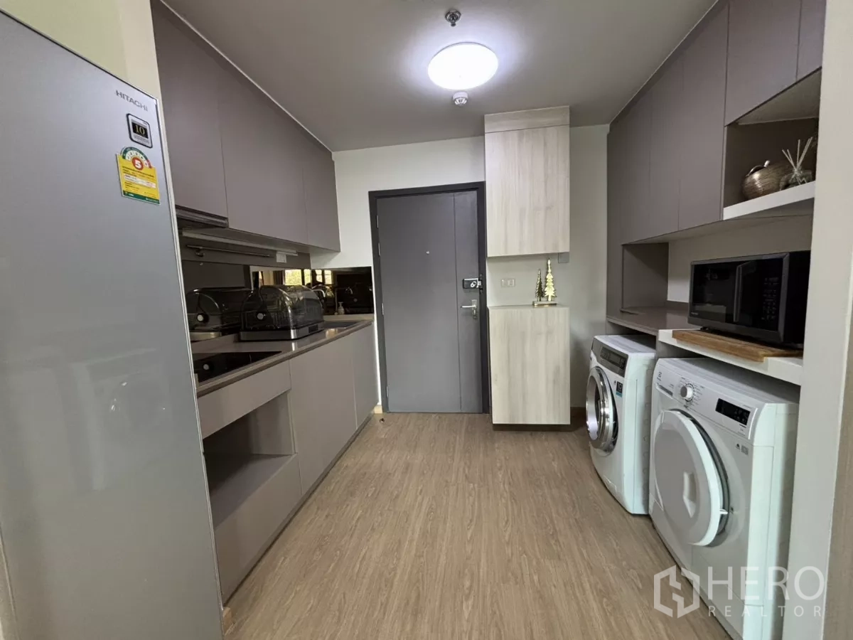 Condominium for rent in Phra Khanong, Bangkok - Galley kitchen with sleek cabinetry, cooktop, sink and built-in laundry appliances.