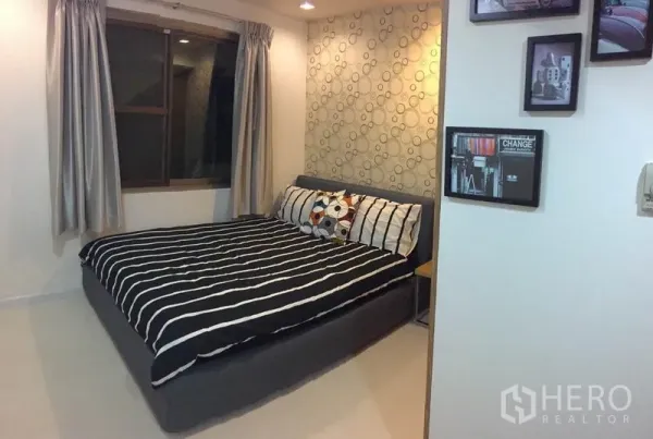 Condominium for rent or sale in Watthana, Bangkok - Cozy bedroom with striped bedding, accent wallpaper and window with curtains.