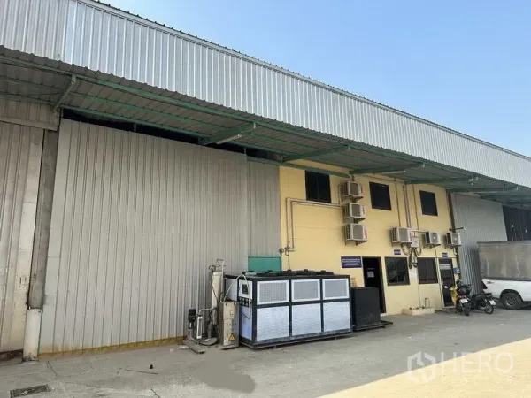 工厂 出租在Khlong Luang, Pathum Thani - 空銮工厂外立面，金属板墙体，带雨棚装卸区、空调机组与停车位。