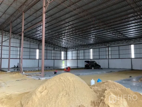 Warehouse for rent or sale in Sai Noi, Nonthaburi - Wide-span interior showing sand piles and a steel roof with ventilation louvers.