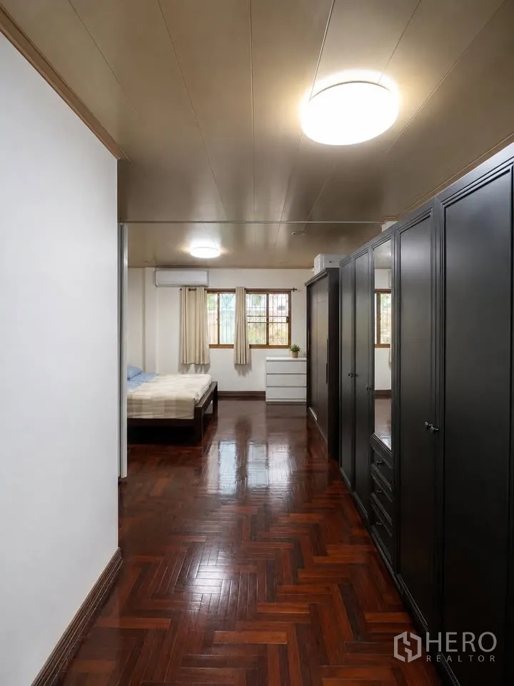 Detached House for rent in Prawet, Bangkok - Long room with black wardrobes, bed and glossy herringbone parquet.