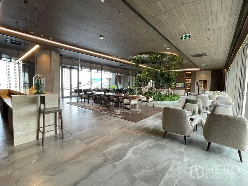 Condominium for rent in Samut Prakan - Co-working and social area with long tables, soft seating and indoor greenery.