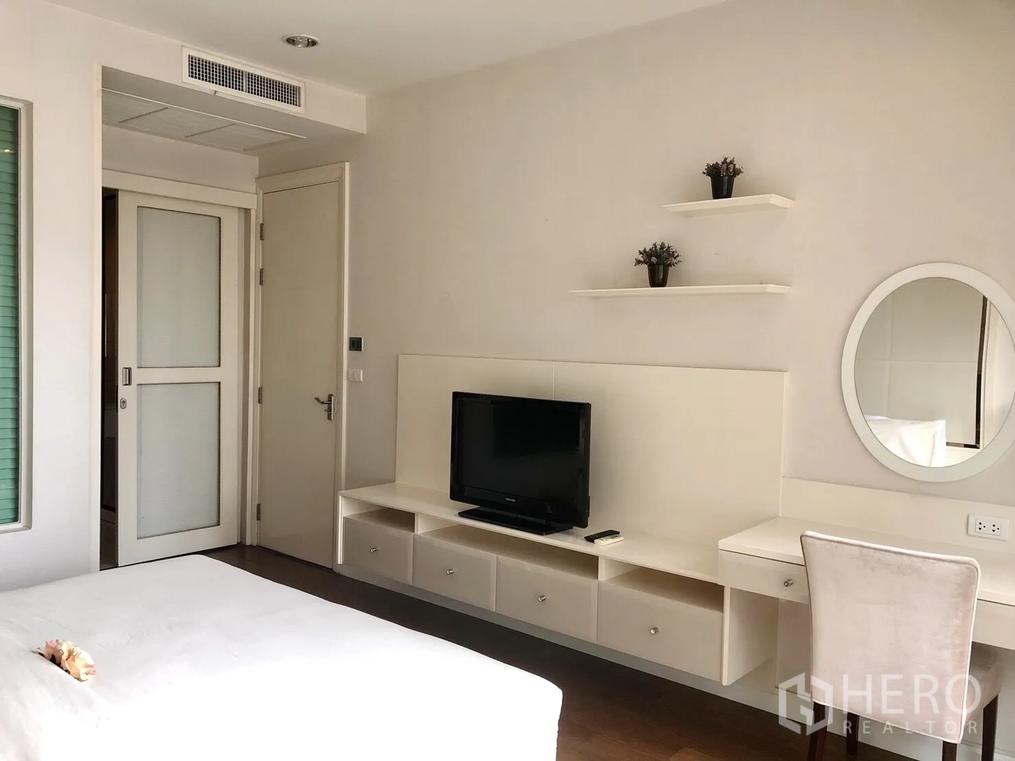 公寓 出租在Pathum Wan, Bangkok - 卧室带内置书妆一体桌与搁板，墙挂电视，配色柔和。