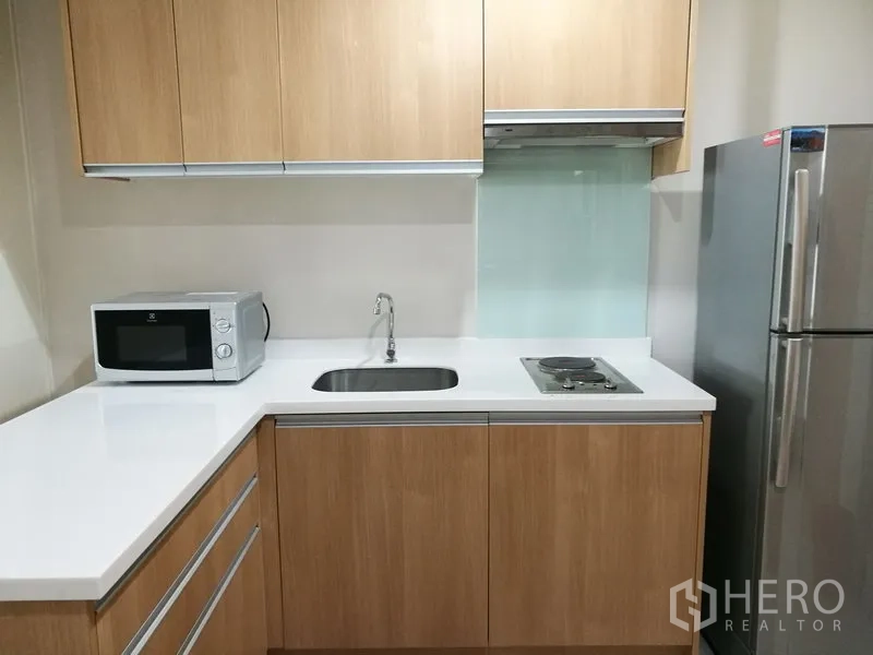 คอนโด ให้เช่าในRatchathewi, Bangkok - ครัวรูปตัว U ตู้ลายไม้ ท็อปสีขาว เตาไฟ เครื่องดูดควัน ไมโครเวฟ และตู้เย็น