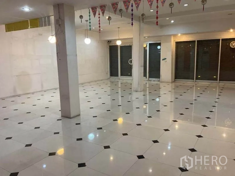 店屋 出租在Suan Luang, Bangkok - 店屋开放式内部，白色亮面地砖、立柱、吊灯与大面积玻璃门面及卷闸门。