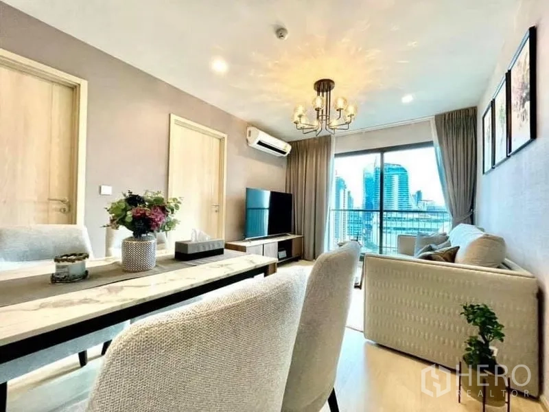 Condominium for rent in Pathum Wan, Bangkok - Living and dining space with TV console, sofa and sliding glass doors to balcony.
