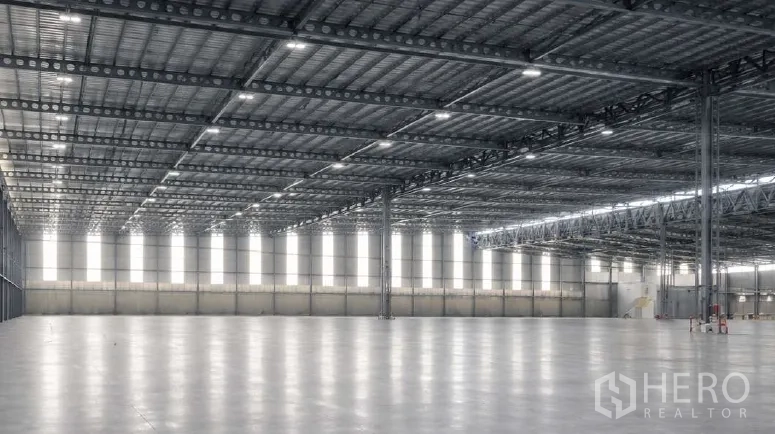 Factory for rent in Bang Pakong, Chachoengsao - Spacious warehouse interior with high steel truss ceiling, bright lighting, and polished concrete floor.