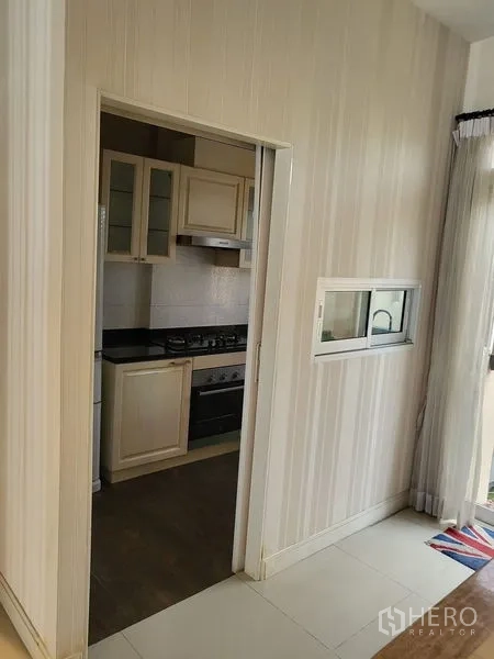 Townhouse for rent in Wang Thonglang, Bangkok - Semi-enclosed kitchen with sliding door, gas hob and cream cabinets.