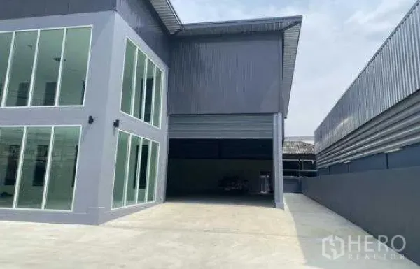 货栈 出租在Prawet, Bangkok - 玻璃办公楼旁的大型卷闸门与有顶装卸区，车道宽敞便于卡车进出。