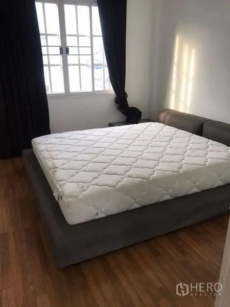 Townhouse for rent in Bang Kapi, Bangkok - Bedroom with platform bed, large window, blackout curtains, and wood flooring.