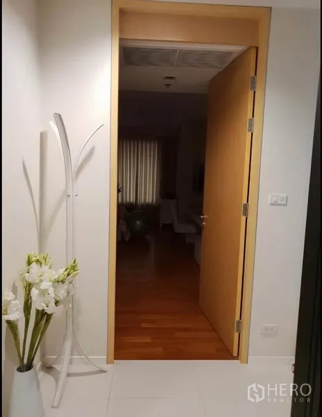 公寓 出租在Sathon, Bangkok - 入户走廊，木门开启，白色地砖与装饰花瓶。