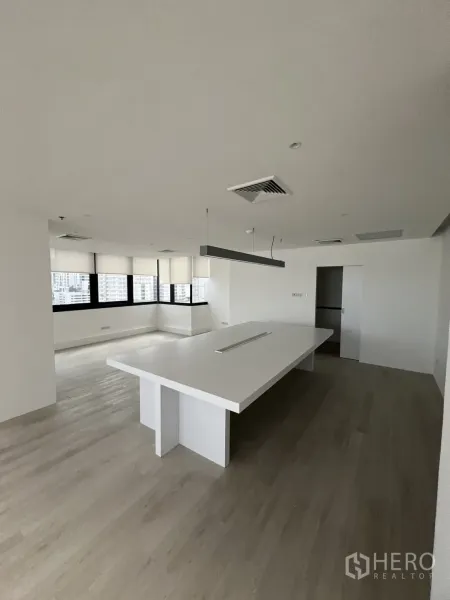 Office Space for rent in Khlong Toei, Bangkok - Open office area featuring a large white island table, pendant light and wide black‑framed windows.