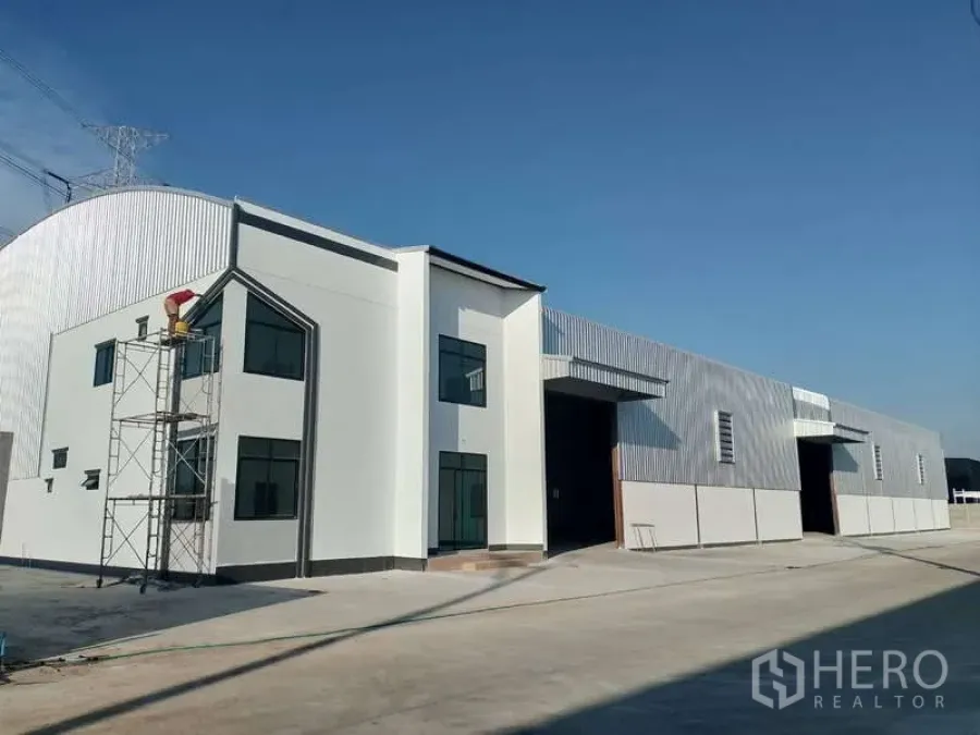 工厂 出租或出售在Sai Noi, Nonthaburi - 新建工厂外观，带两层办公室、宽大卷帘门与混凝土前院，天空晴朗。
