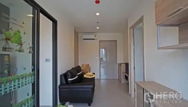 Condominium for rent in Khlong Toei, Bangkok - Bright corridor-style living room with leather sofa, shelving and recessed ceiling lights.