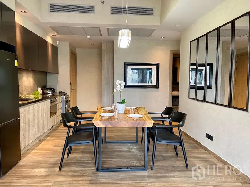 Condominium for rent in Watthana, Bangkok - Open-plan dining area with wooden table for four beside a modern kitchen and wall mirrors.