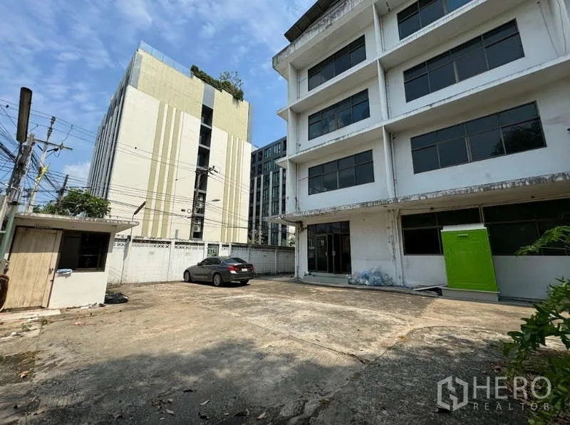 Home Office for sale in Bang Na, Bangkok - Spacious forecourt parking area inside a walled compound beside neighboring buildings.