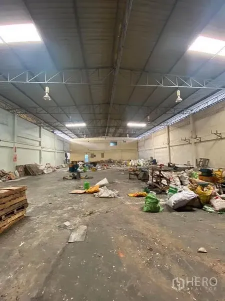 工厂 出租在Samut Sakhon - 宽阔厂房，钢结构屋顶与天窗，工业照明，混凝土地面，现场堆放物料。