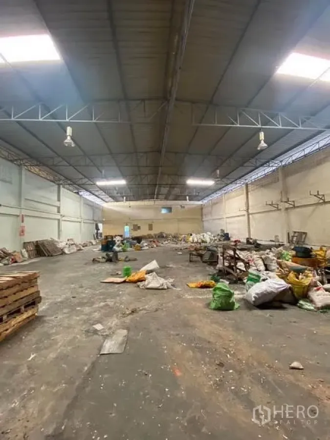 工厂 出租在Samut Sakhon - 宽阔厂房，钢结构屋顶与天窗，工业照明，混凝土地面，现场堆放物料。