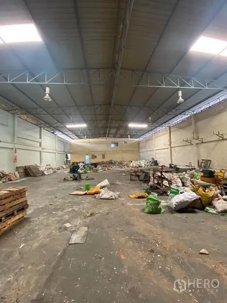 工厂 出租在Samut Sakhon - 宽阔厂房，钢结构屋顶与天窗，工业照明，混凝土地面，现场堆放物料。