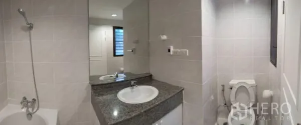 Condominium for rent in Sathon, Bangkok - Bright tiled bathroom with bathtub, granite vanity and large mirror in Sathon condo.