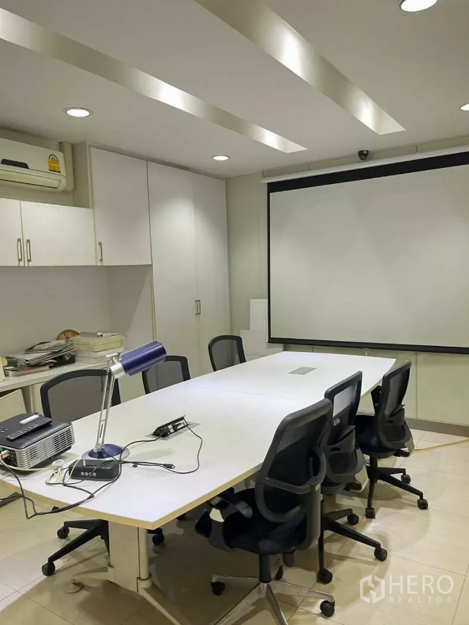 Home Office for rent in Khlong Toei, Bangkok - Modern meeting room with long conference table, projector, screen and built-in cabinets under recessed lighting.