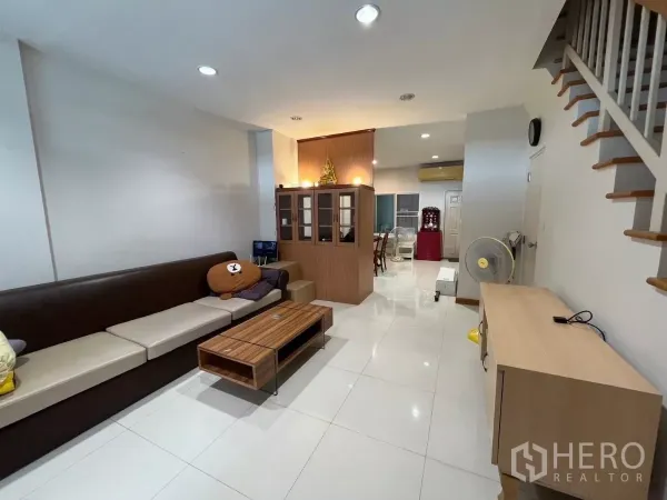 Townhouse for rent in Bang Kho Laem, Bangkok - Bright living room with long sofa, wooden staircase, and glossy tiled flooring.
