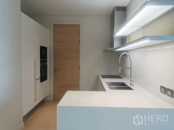Condominium for rent in Pathum Wan, Bangkok - Sleek white kitchen with peninsula, double sink, induction hob and illuminated shelves.
