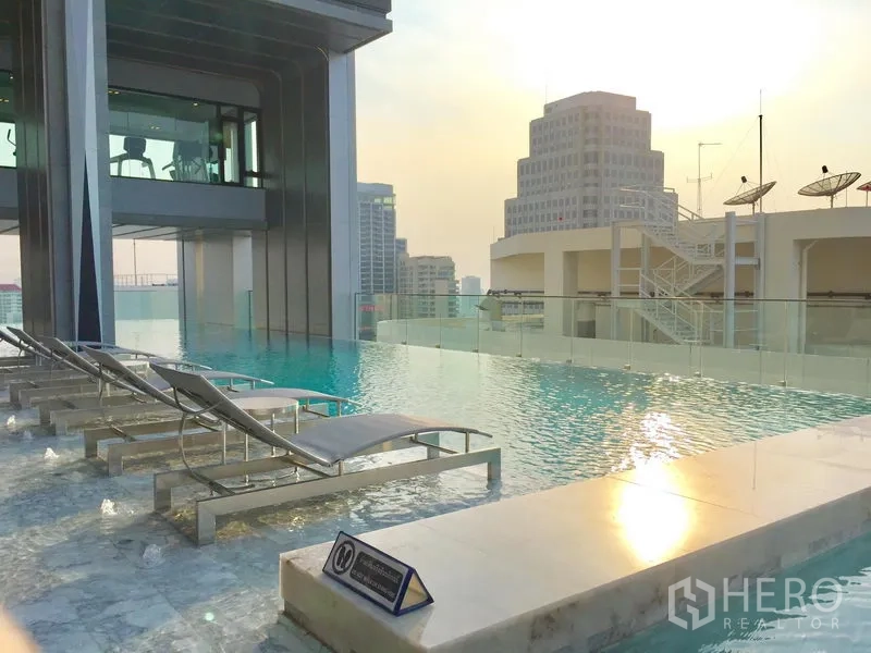 公寓 出租在Watthana, Bangkok - 屋顶无边际泳池，躺椅与城市天际线夕阳景观。