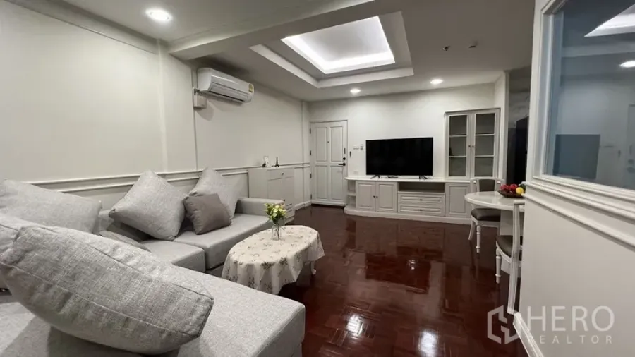Apartment for rent in Watthana, Bangkok - Bright living room with L-shaped gray sofa, tray ceiling, TV console and glossy parquet floors.