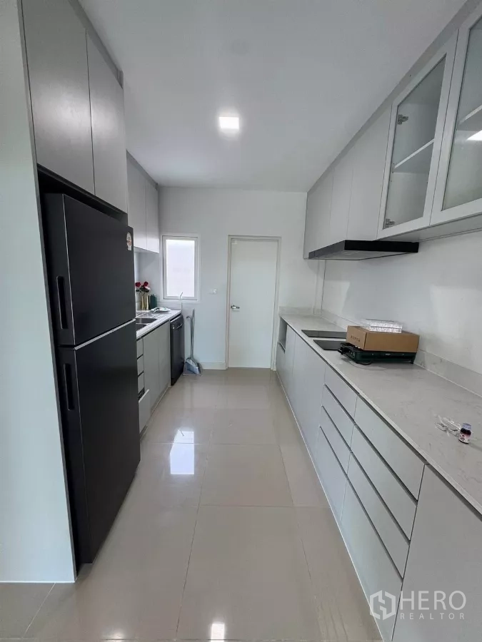 Detached House for rent in Bang Phli, Samut Prakan - Long galley kitchen with tall fridge, cabinets on both sides and glossy floor tiles.