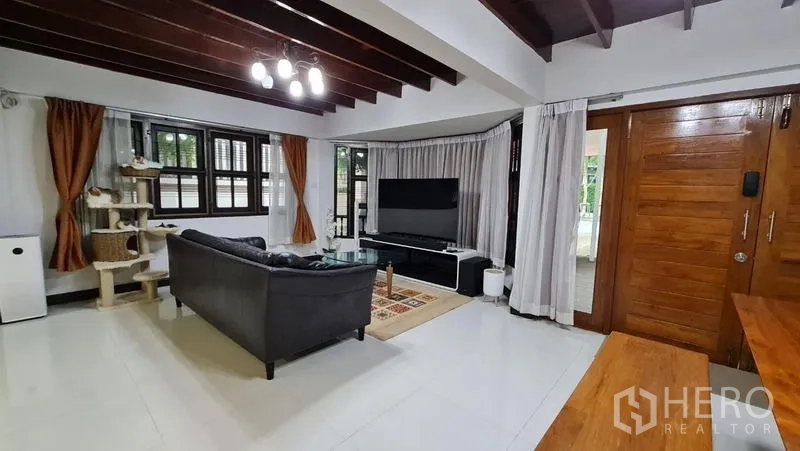 Detached House for rent in Saphan Sung, Bangkok - Living room with sofa, large TV console, and corner windows with curtains.