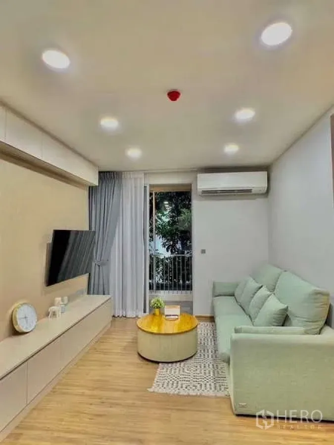 Condominium for sale in Watthana, Bangkok - Bright living room at Q Prasarnmit with mint sofa, wall-mounted TV and balcony view.