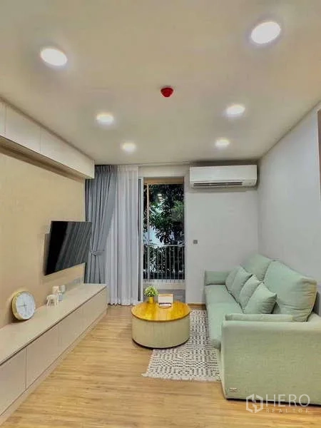 Condominium for sale in Watthana, Bangkok - Bright living room at Q Prasarnmit with mint sofa, wall-mounted TV and balcony view.