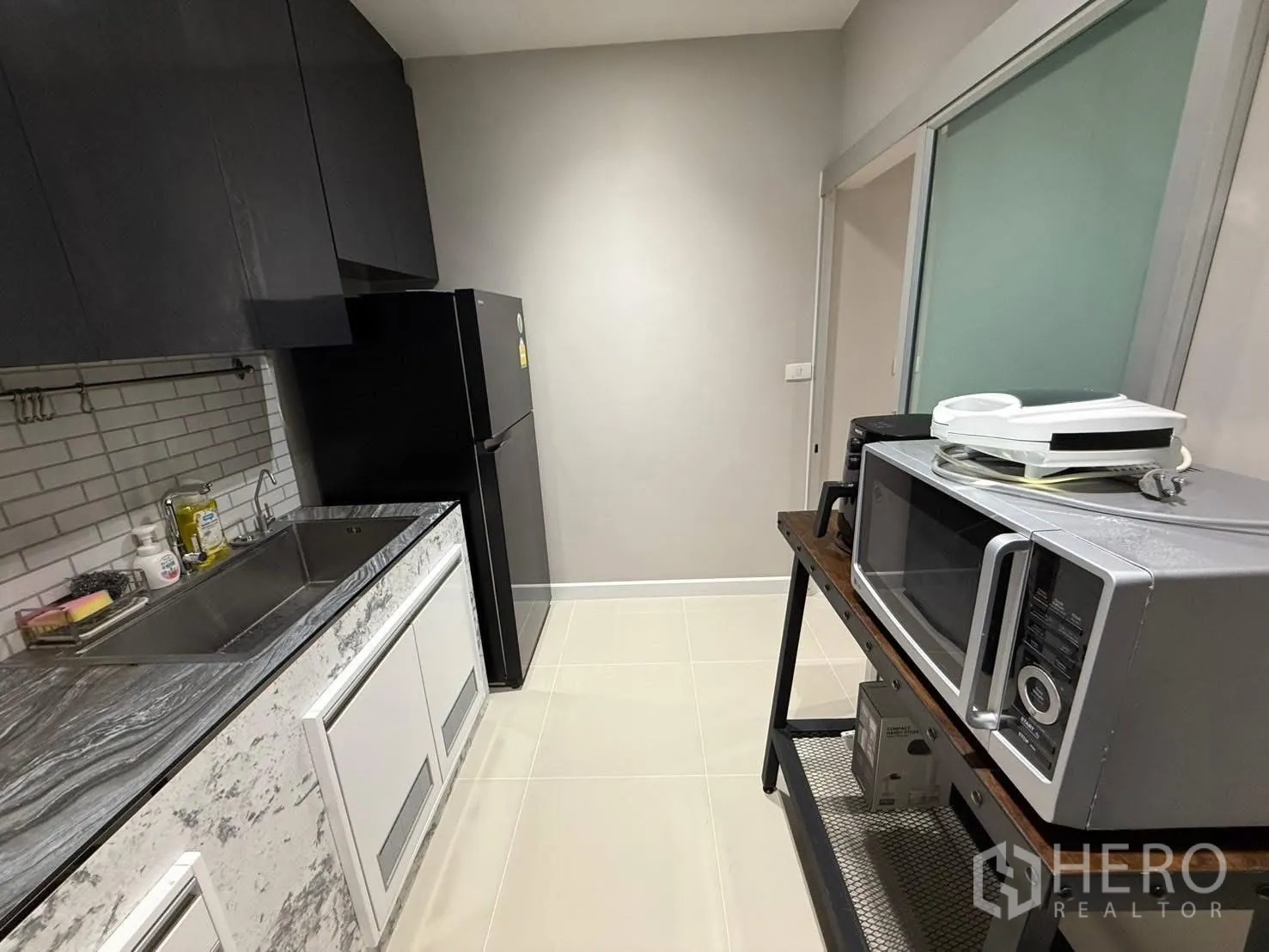 Detached House for rent in Prawet, Bangkok - Compact enclosed kitchen with marble-look countertop, stainless sink, dark cabinetry and microwave on side rack.