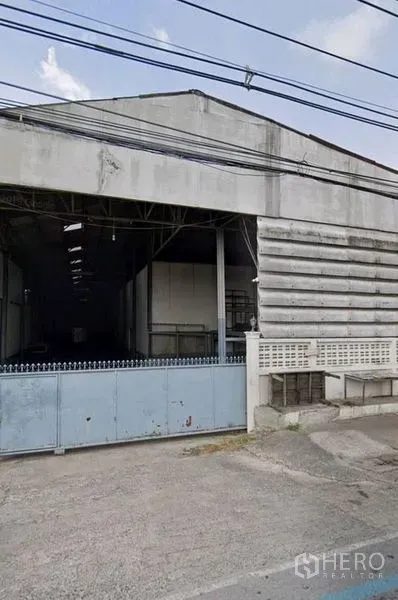 货栈 出租在Pathum Thani - 临街仓库外立面，宽幅滑动大门与混凝土车道，位于巴吞他尼市区。
