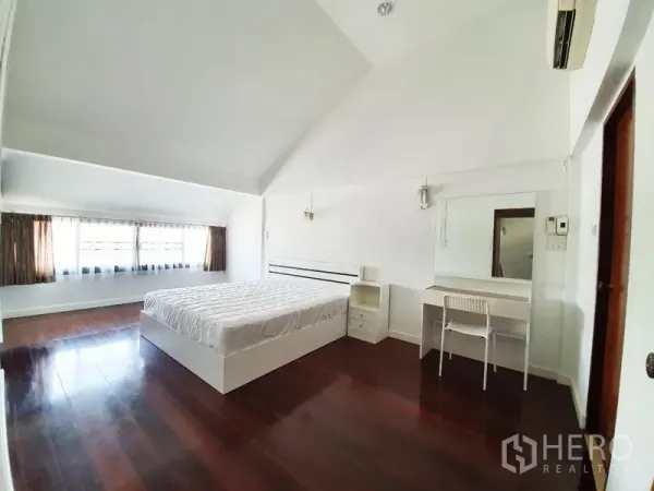 独立式住宅 出租在Phra Khanong, Bangkok - 高挑卧室，深色木地板，大窗采光，白墙，床与梳妆台，空调。