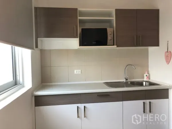 Condominium for rent in Huai Khwang, Bangkok - Bright compact kitchen with white countertop, tiled backsplash, upper cabinets, microwave, and stainless sink.