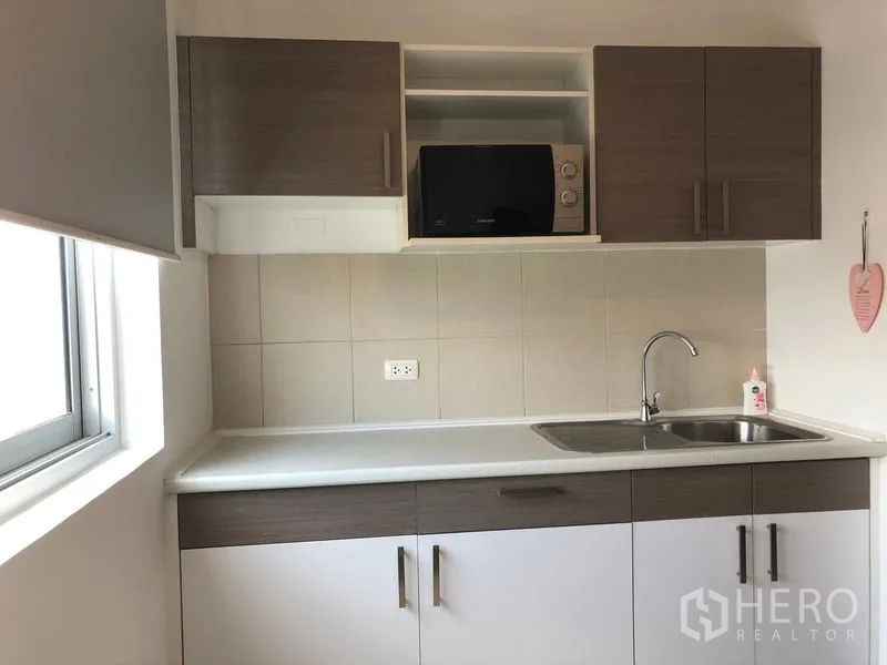 Condominium for rent in Huai Khwang, Bangkok - Bright compact kitchen with white countertop, tiled backsplash, upper cabinets, microwave, and stainless sink.
