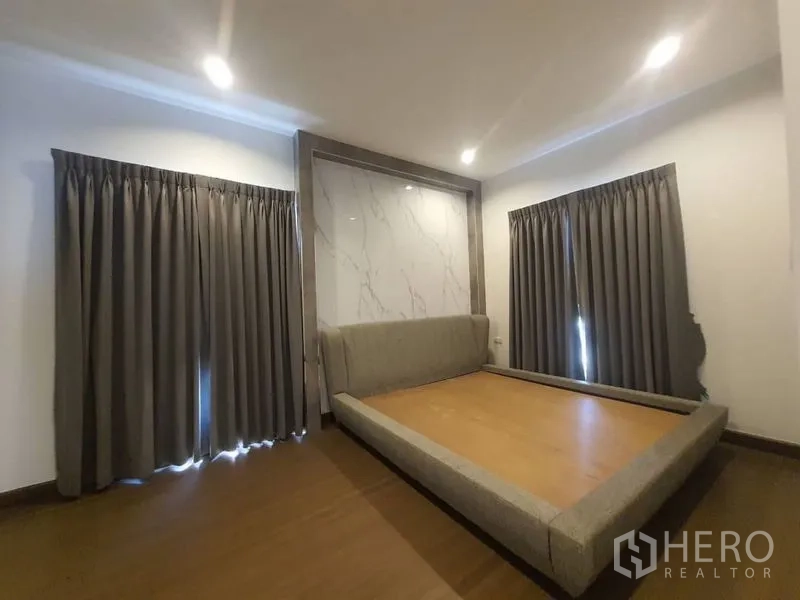 Detached House for rent in Prawet, Bangkok - Bedroom with platform bed frame, marble feature wall, wood floor and dark curtains.