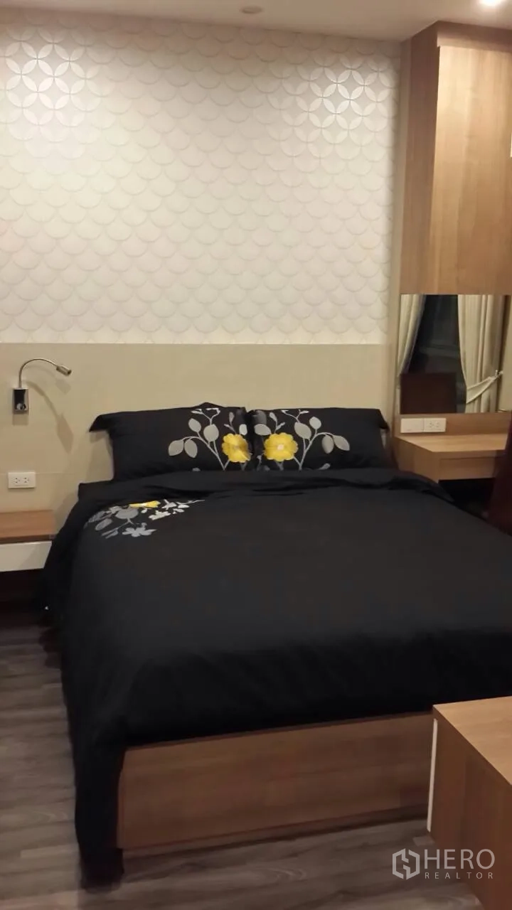 Condominium for rent in Mueang Samut Prakan, Samut Prakan - Second bedroom featuring a platform bed, patterned accent wall, bedside lighting, and warm wood furnishings.