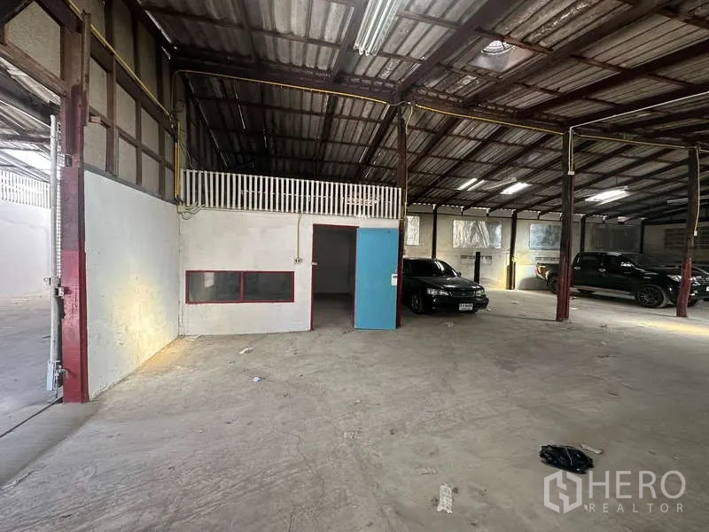 Warehouse for rent in Suan Luang, Bangkok - Warehouse interior showing a small office cabin with a blue door, mezzanine-style railing and fluorescent lighting.