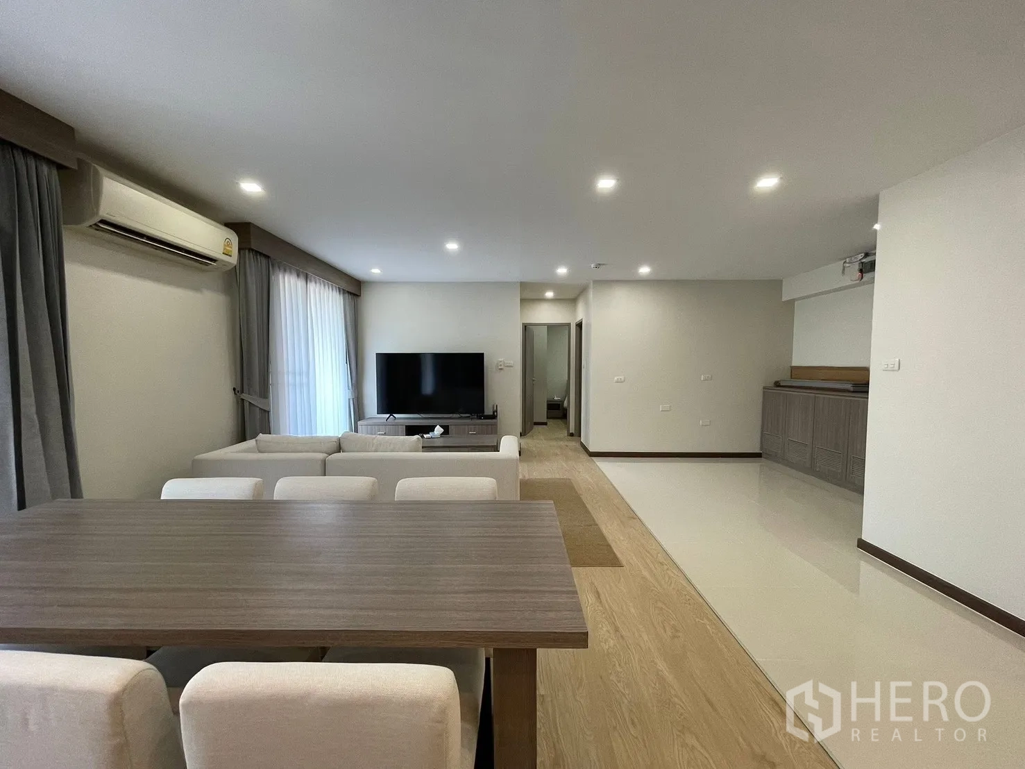 Condominium for rent in Watthana, Bangkok - Spacious lounge with L-shaped sofa, large TV, and a long dining table in a bright open-plan interior.
