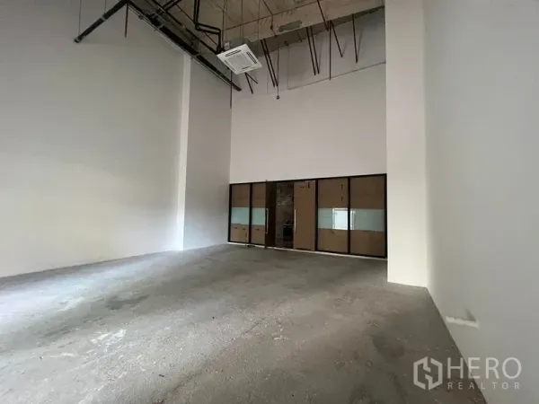 零售空间 出租在Bang Kapi, Bangkok - 空置零售铺面，双层挑高天花，外露管线，后方为玻璃隔间。