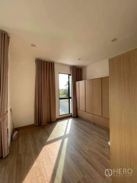Townhouse for rent or sale in Bang Kapi, Bangkok - Bedroom with wardrobes, tall windows, curtains and warm natural light.