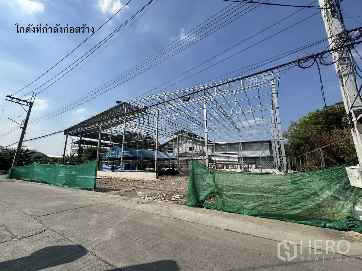 คลังสินค้า ให้เช่าในBang Kapi, Bangkok - โครงสร้างเหล็กโกดังระหว่างก่อสร้างริมถนน มีเสาไฟและตาข่ายกันฝุ่นสีเขียว