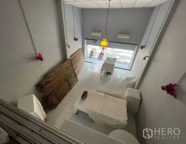 อาคารพาณิชย์ ให้เช่าในWatthana, Bangkok - มุมมองจากชั้นลอยลงสู่โถงหน้าร้านเพดานสูง พร้อมโคมไฟแขวนและผนังสีเทา