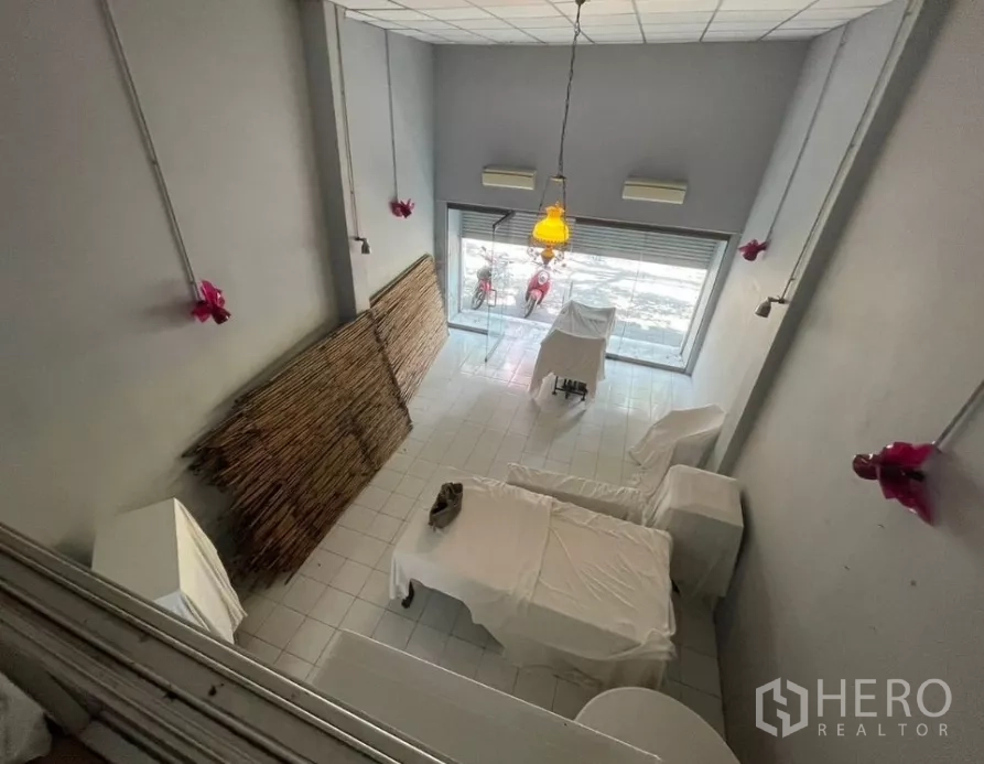 อาคารพาณิชย์ ให้เช่าในWatthana, Bangkok - มุมมองจากชั้นลอยลงสู่โถงหน้าร้านเพดานสูง พร้อมโคมไฟแขวนและผนังสีเทา