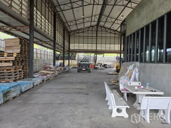 Warehouse for sale in Lat Lum Kaeo, Pathum Thani - High-clearance warehouse interior with steel trusses, concrete floor, pallet storage and long windowed office wall.