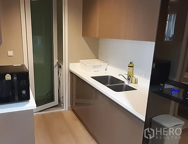 คอนโด ให้เช่าในKhlong Toei, Bangkok - ครัวรูปแบบแกลเลย์ เคาน์เตอร์สีขาว อ่างล้างจานคู่ ตู้เก็บของ และไมโครเวฟ